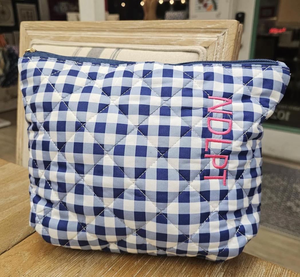 Quilted pouch with blue and white check pattern and 'NDLPT' embroidery on a wooden surface.