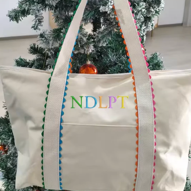Beige tote bag with colorful trim and 'NDLPT' text in front of a decorated Christmas tree.