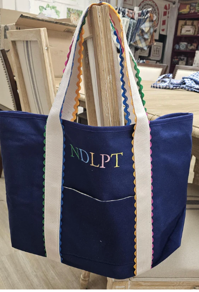 Blue tote bag with colorful trim and 'NDLPT' embroidery in a room setting.