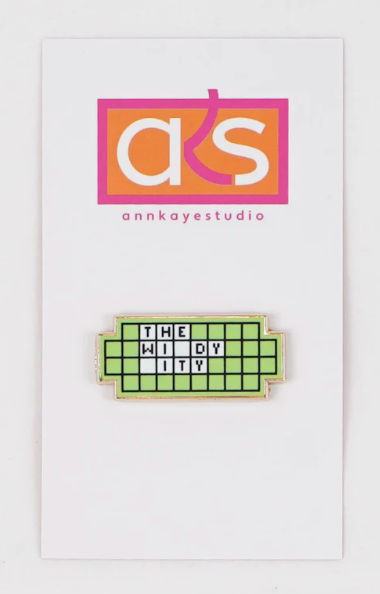 Enamel pin with 'The Widyity' design on a card with 'annkayestudio' branding.